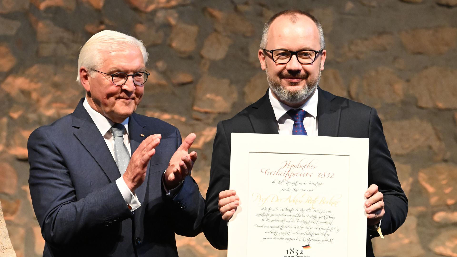 Die beiden stehen nebeneinander vor einer Steinwand. Bodnar hält lächenldn die Preisurkunde vor sich; Steinmeier applaudiert.