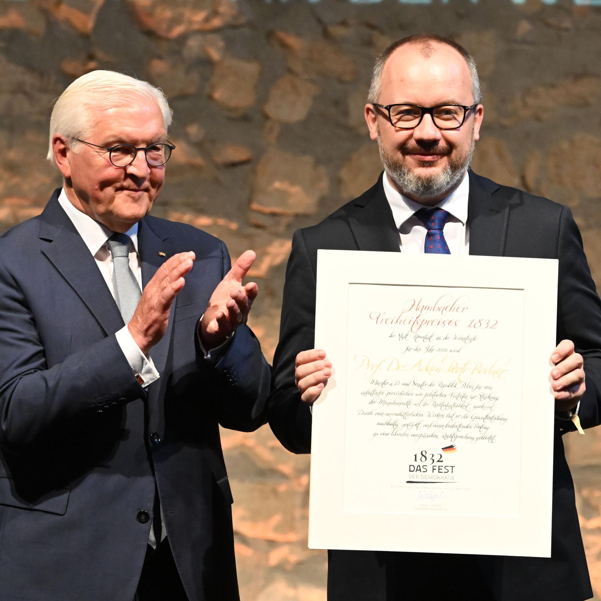 Die beiden stehen nebeneinander vor einer Steinwand. Bodnar hält lächenldn die Preisurkunde vor sich; Steinmeier applaudiert.