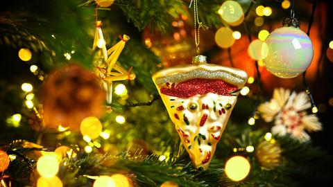 Weihnachtsschmuck in Form eines Pizzastücks hängt an einem Weihnachtsbaum