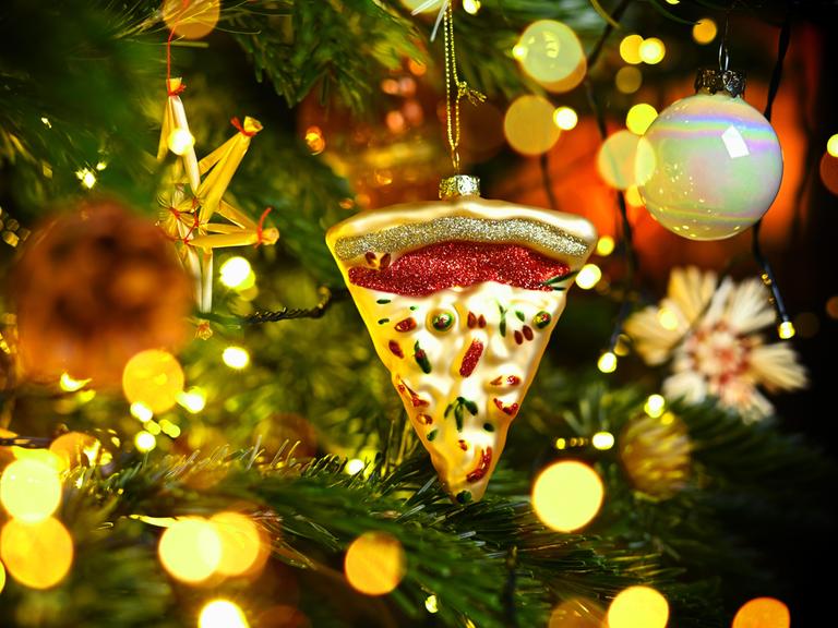 Weihnachtsschmuck in Form eines Pizzastücks hängt an einem Weihnachtsbaum