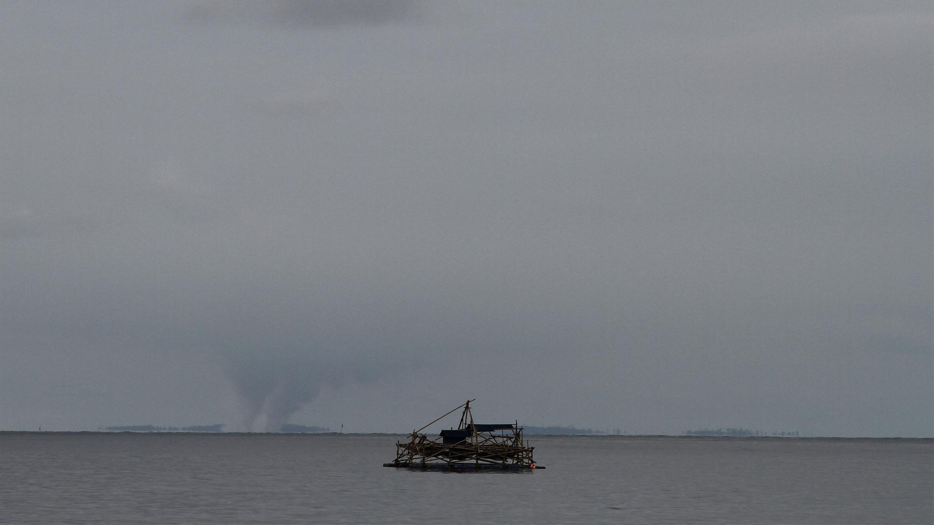 Der Vulkan Krakatau aus großer Entfernung fotografiert. Man sieht zwei Aschesäulen. Im Vordergrund ein Fischerboot auf dem Wasser. Der Vulkan Krakatau aus großer Entfernung fotografiert. Man sieht zwei Aschesäulen. Im Vordergrund ein Fischerboot auf dem Wasser.