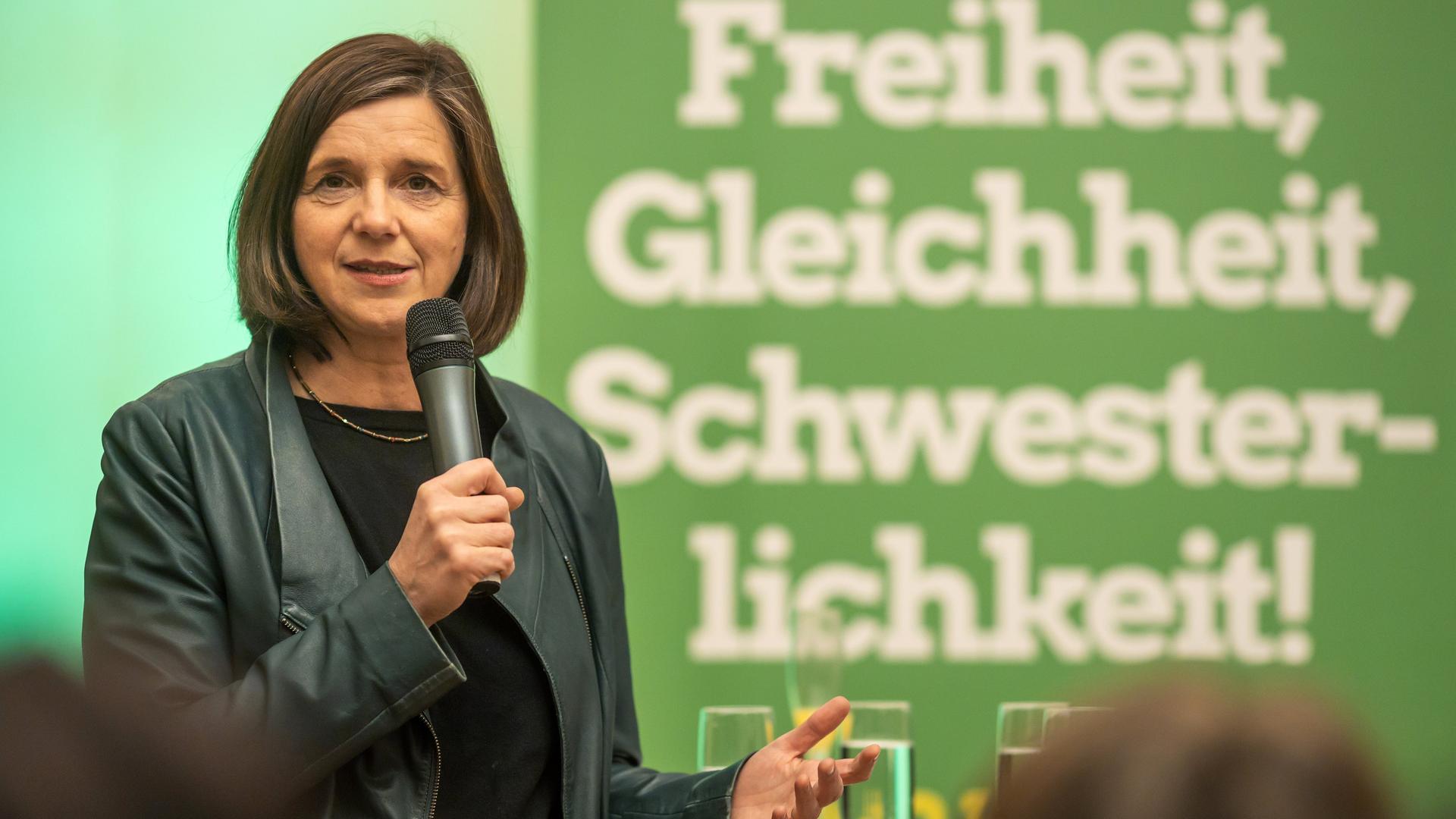 Die grüne Spitzenpolitikerin Kathrin Göring-Eckhardt hat ein Mikrophon in der Hand und steht vor einem grünen Plakat mit der Aufschrift "Freiheit, Gleichheit, Schwesterlichkeit".