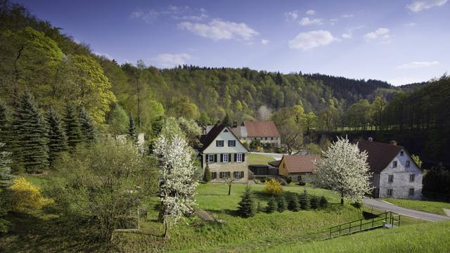 Ein Dorf liegt in hügeliger, grüner Landschaft.