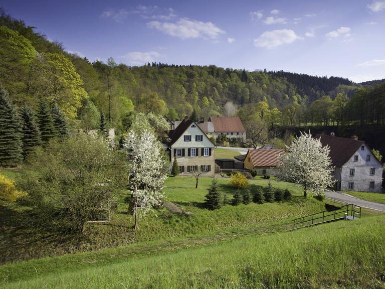 Ein Dorf liegt in hügeliger, grüner Landschaft.