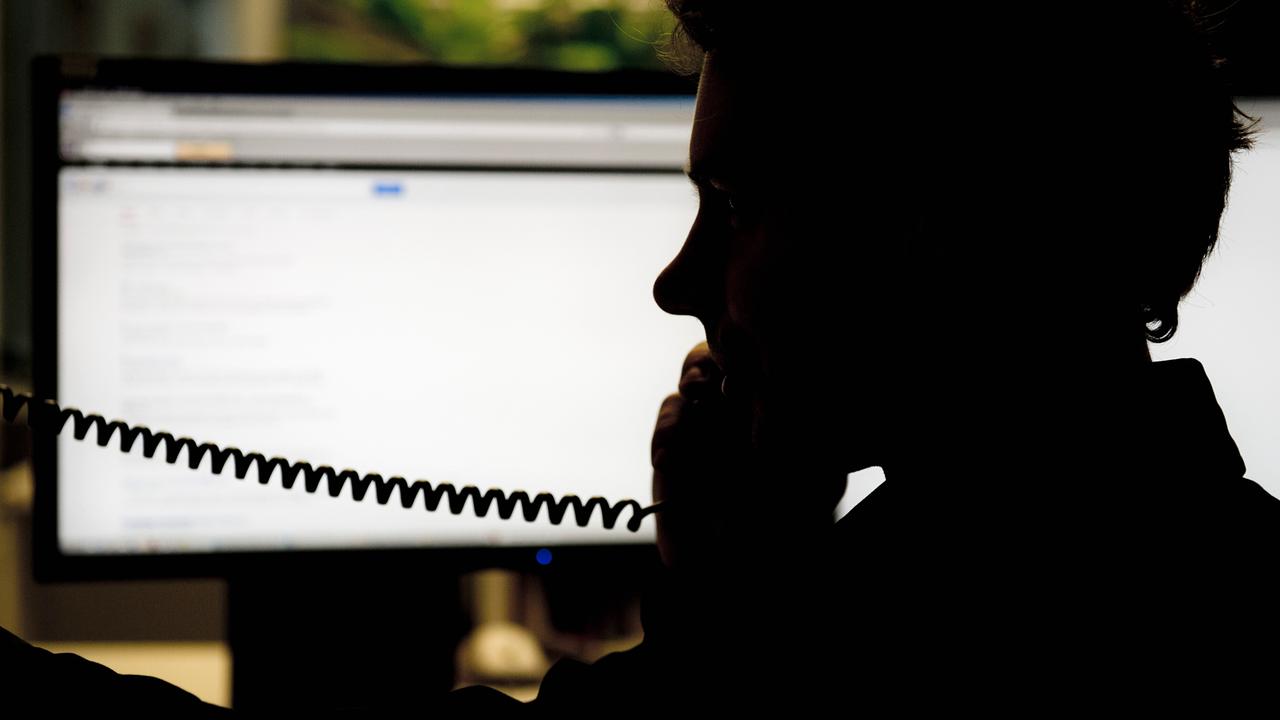 Schatten eines Mannes, der über ein Festnetz-Telefon telefoniert. Im Hintergrund leuchtet ein Computerbildschirm.