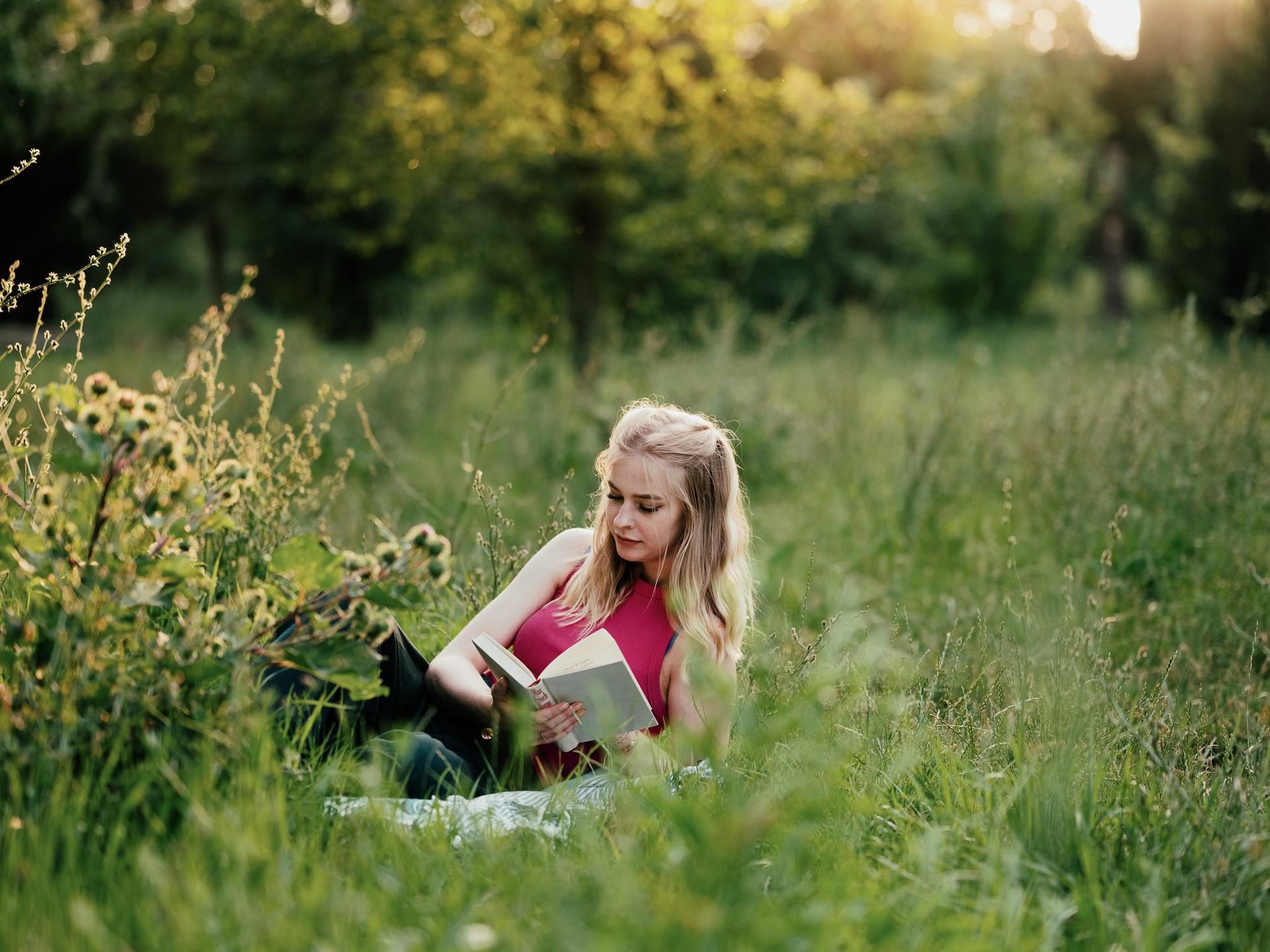 Eine Frau liegt in einer Sommerwiese und liest ein Buch