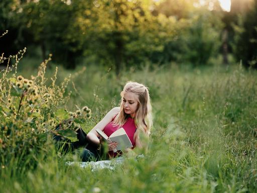 Eine Frau liegt in einer Sommerwiese und liest ein Buch