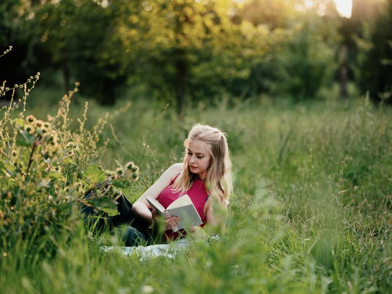 Eine Frau liegt in einer Sommerwiese und liest ein Buch Eine Frau liegt in einer Sommerwiese und liest ein Buch