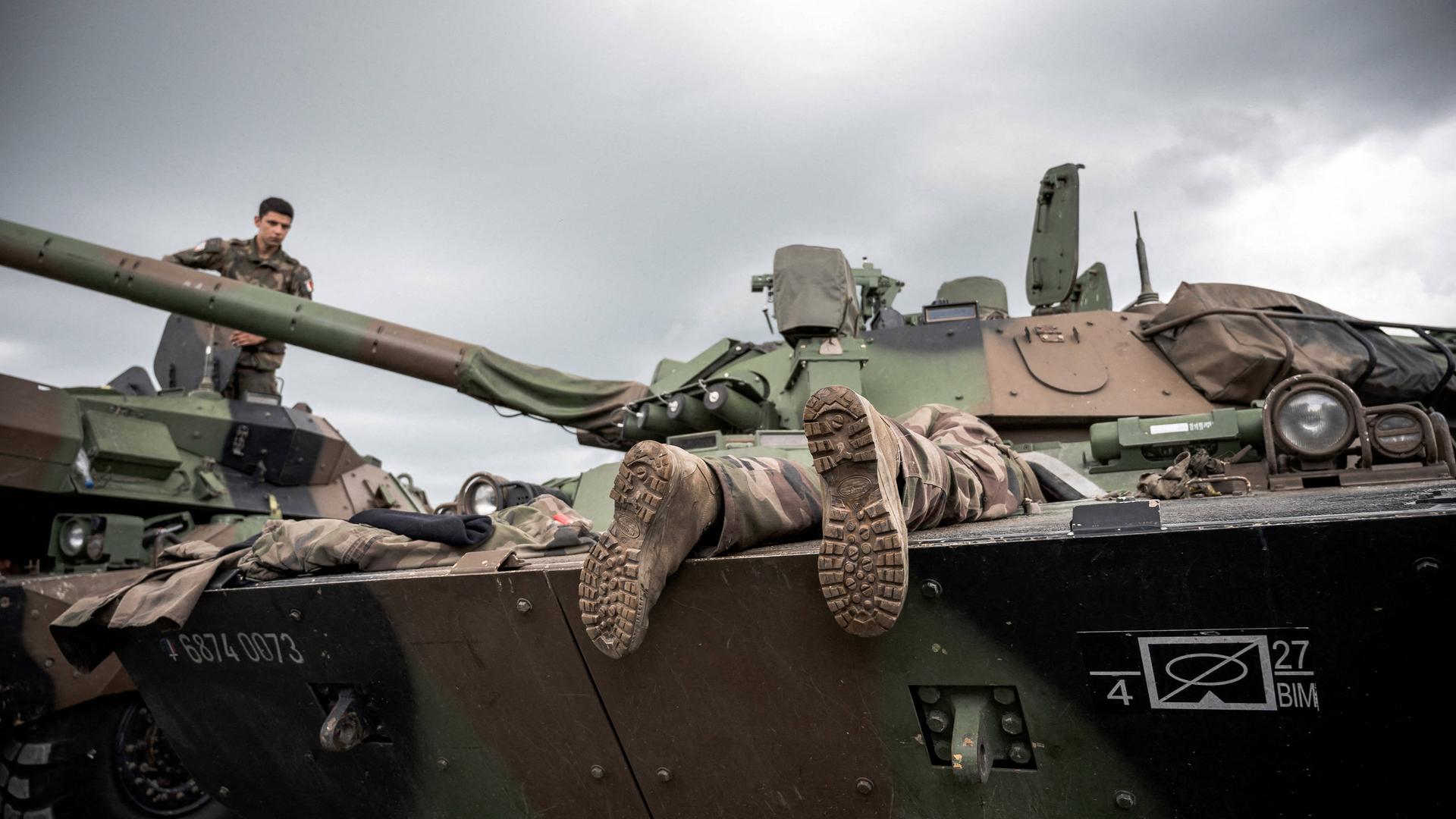 Aus einem Panzer schauen zwei Beine heraus. An diesen sind Soldatenstiefel. 