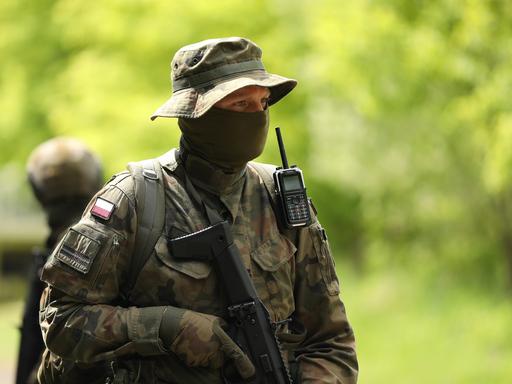 Ein vermummter polinischer Soldat trägt Uniform, Schlapphut und einen schwazren Schal vor seinem Gesicht