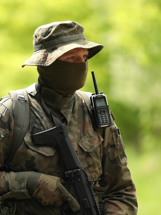 Ein vermummter polinischer Soldat trägt Uniform, Schlapphut und einen schwazren Schal vor seinem Gesicht