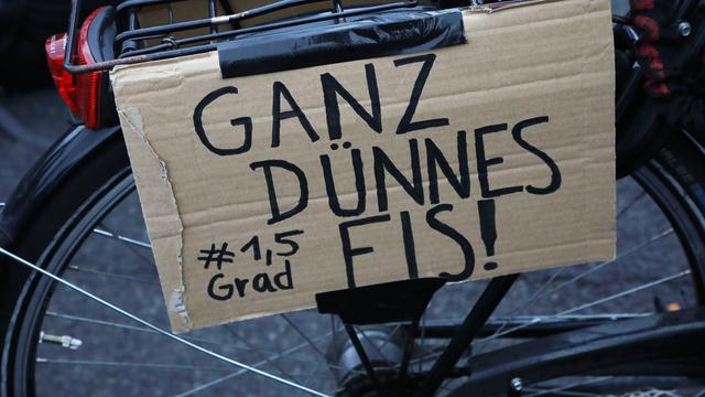 Protestschild mit der Aufschrift "Ganz dünnes Eis #1,5Grad" hängt am Gepäckträger eines Fahrrads.