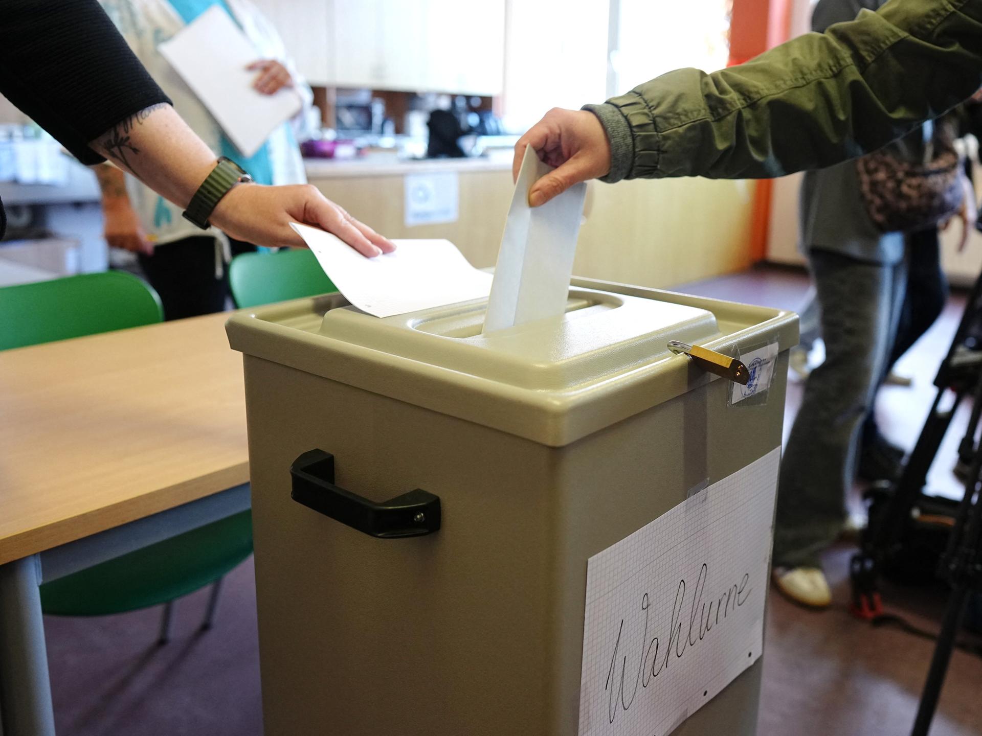 Ein Wähler wirft seinen gefalteten Stimmzettel in die Wahlurne in einem Wahllokal. Ein Wähler wirft seinen gefalteten Stimmzettel in die Wahlurne in einem Wahllokal.