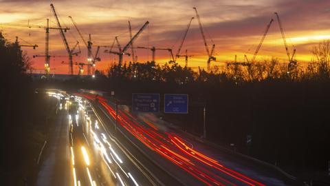 Die Baustelle des ESMC-Chipfabrik: Daran vorbei fahren in der Dämmerung die Autos auf der Autobahn. Die Lichter sind als weiße und rote Schweife zu erkenne. Im Hintergrund stehen Krähne der Baustelle. 