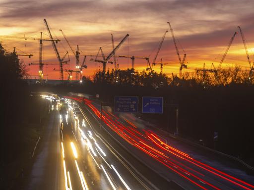 Baustelle der ESMC-Chipfabrik: Daran vorbei fahren in der Dämmerung Autos auf der Autobahn. Die Lichter sind als weiße und rote Schweife zu erkennen. Im Hintergrund stehen Krähne der Baustelle. Baustelle der ESMC-Chipfabrik: Daran vorbei fahren in der Dämmerung Autos auf der Autobahn. Die Lichter sind als weiße und rote Schweife zu erkennen. Im Hintergrund stehen Krähne der Baustelle.