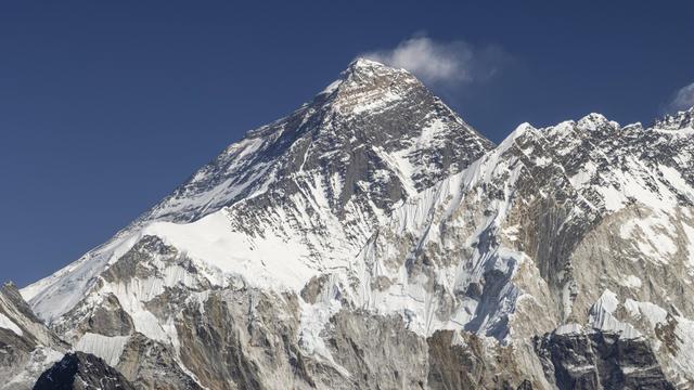 Der Gipfel von dem Mount Everest. Der höchste Berg der Welt liegt im Sonnenlicht. Von seiner Spitze fliegt etwas Schnee davon. 