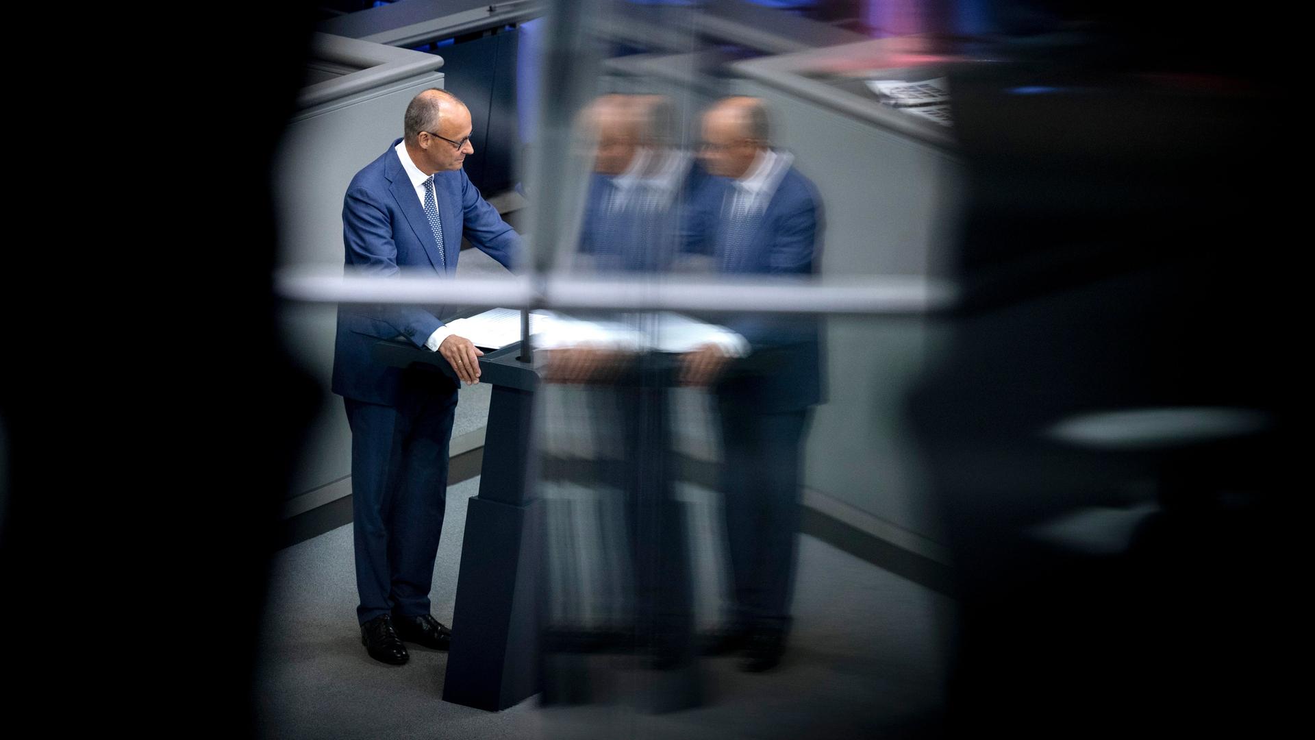 Friedrich Merz steht am Rednerpult im Bundestag. Das Bild spiegelt sich in einer Scheibe. Darum ist alles schwarz.