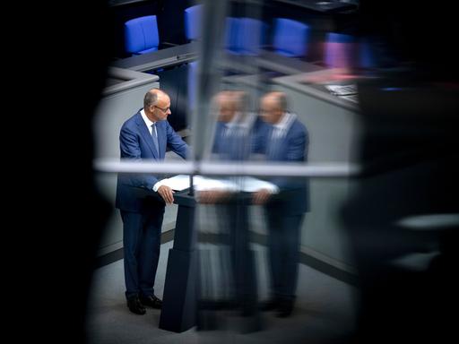 Friedrich Merz steht am Rednerpult im Bundestag. Das Bild spiegelt sich in einer Scheibe. Darum ist alles schwarz. Friedrich Merz steht am Rednerpult im Bundestag. Das Bild spiegelt sich in einer Scheibe. Darum ist alles schwarz.