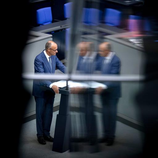 Friedrich Merz steht am Rednerpult im Bundestag. Das Bild spiegelt sich in einer Scheibe. Darum ist alles schwarz.