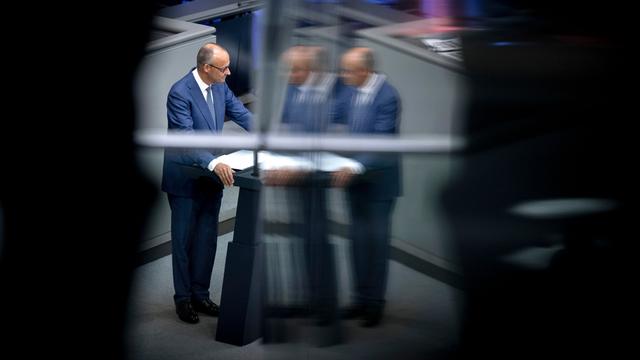 Friedrich Merz steht am Rednerpult im Bundestag. Das Bild spiegelt sich in einer Scheibe. Darum ist alles schwarz.