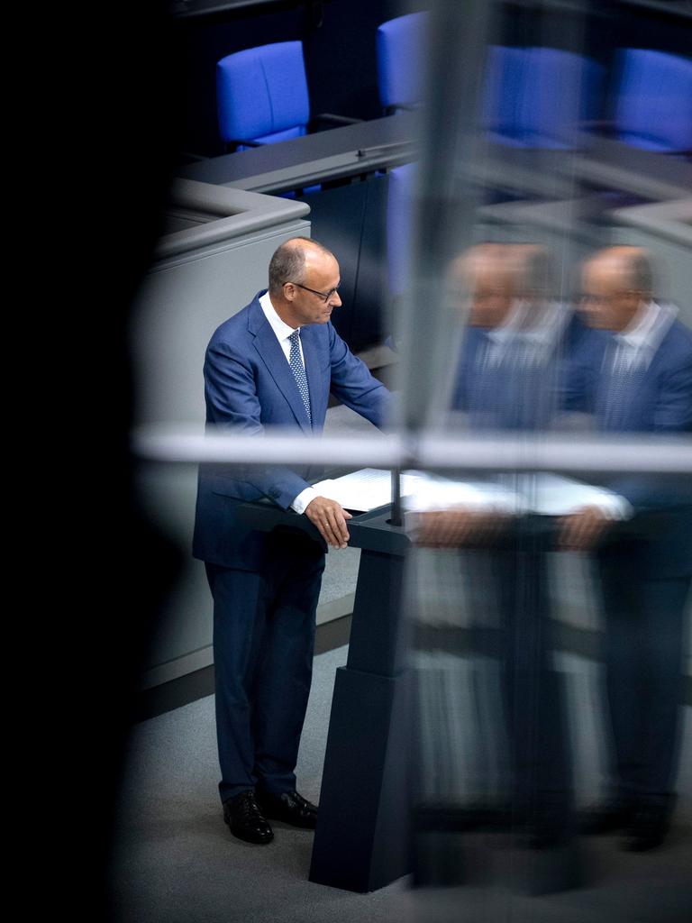 Friedrich Merz steht am Rednerpult im Bundestag. Das Bild spiegelt sich in einer Scheibe. Darum ist alles schwarz. Friedrich Merz steht am Rednerpult im Bundestag. Das Bild spiegelt sich in einer Scheibe. Darum ist alles schwarz.