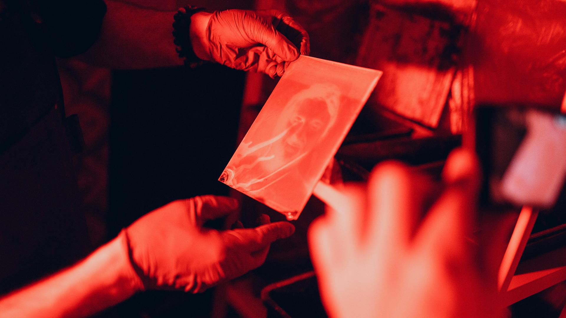 Hände beim Entwickeln von Fotos bei rotem Licht in der Dunkelkammer. Hände beim Entwickeln von Fotos bei rotem Licht in der Dunkelkammer.