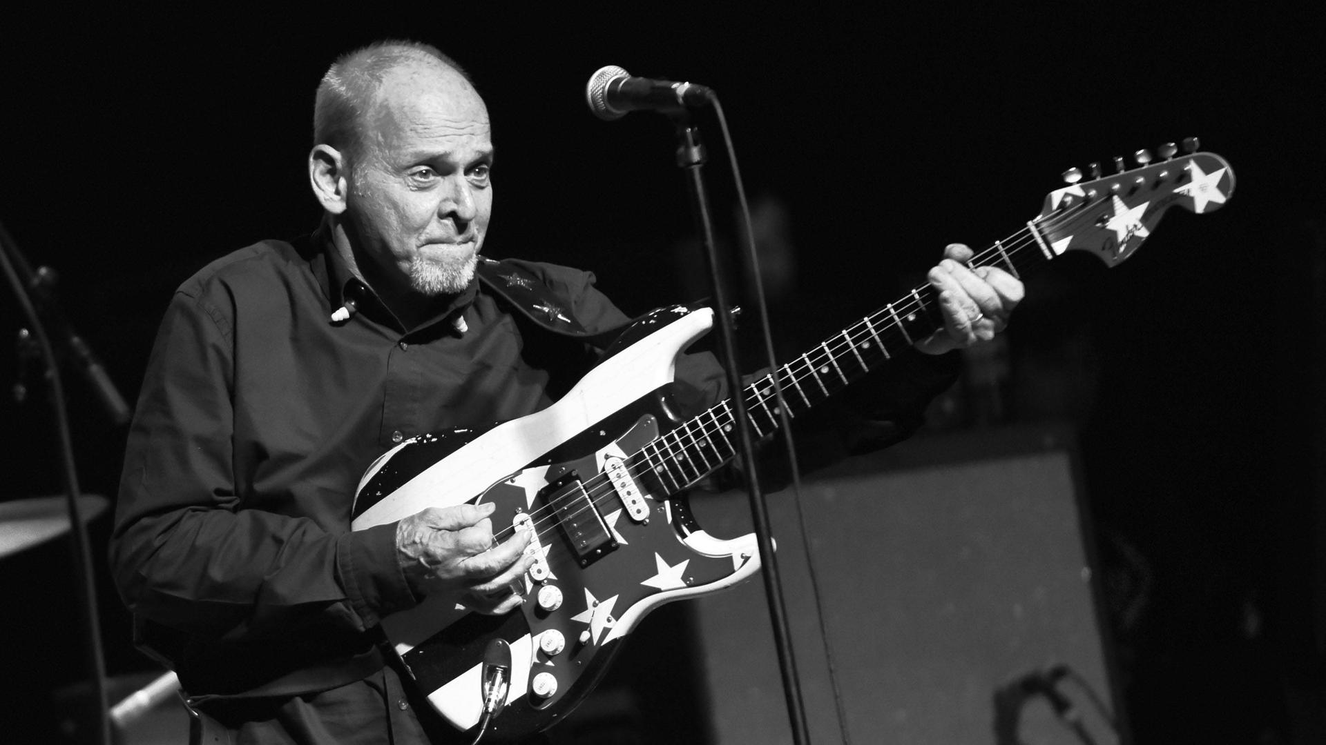 Wayne Kramer von MC5 spielt mit verzerrtem Gesicht und spitzbübischem Grinsen seine Gitarre.