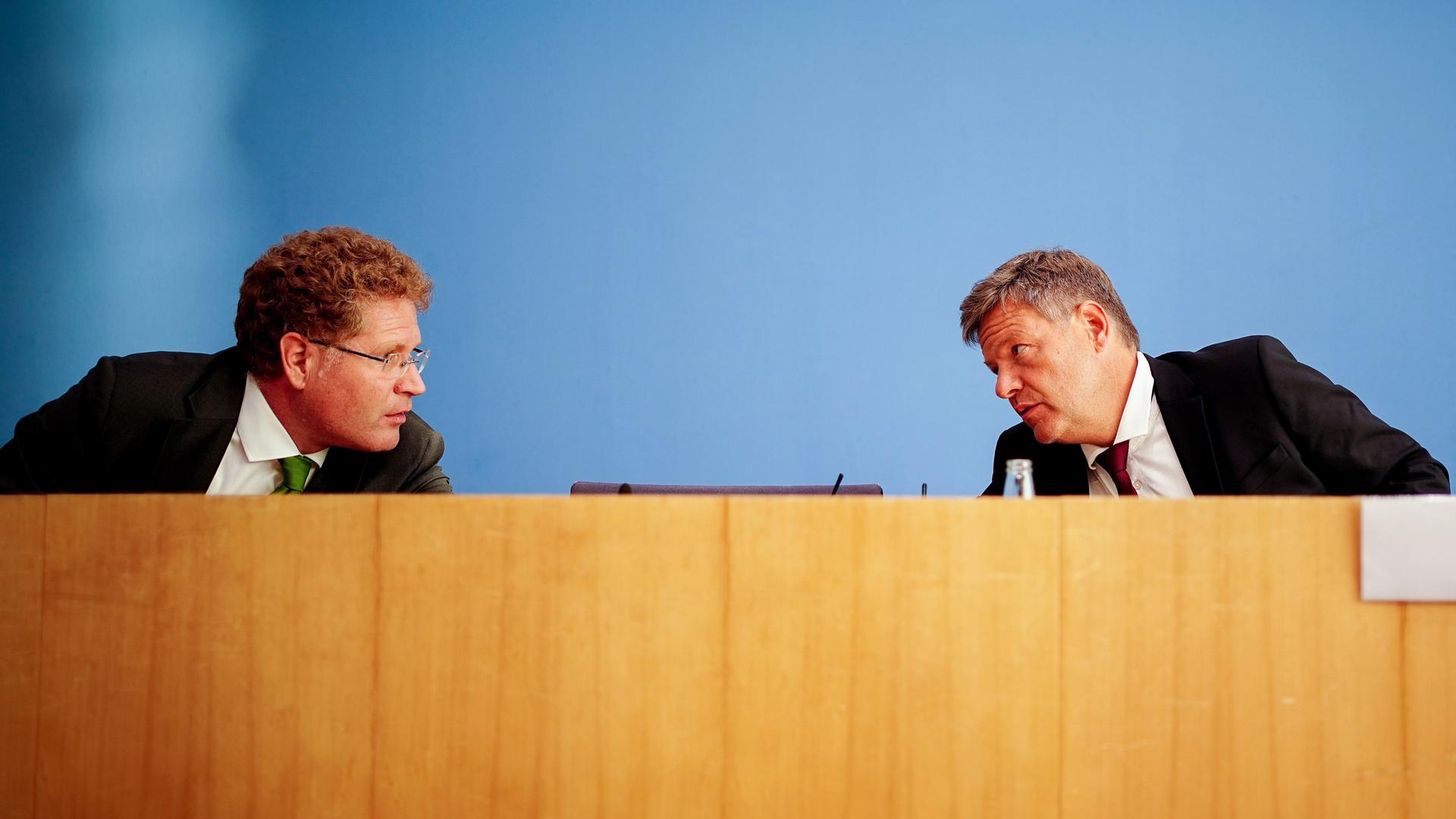 Habeck und Graichen sitzen auf der Bank der Bundespressekonferenz. Beide schauen sich an und sprechen miteinander.
