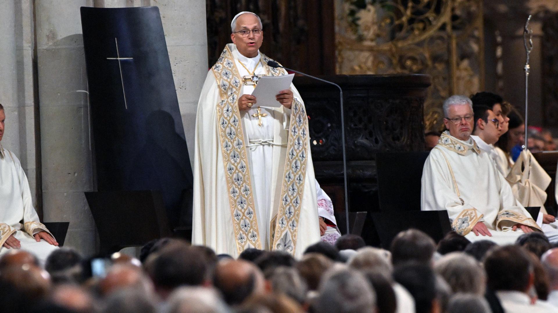 Der Papst während der Andacht in der Kathedrale Notre Dame in Paris - er hält ein Blatt Papier in den Händen und spricht. Am unteren Bildrand sind zahlreiche Besucher von hinten zu sehen.
      
