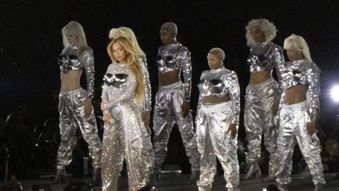 Mehrer Personen stehen in einem Glitzeroutfit auf einer Bühne.  