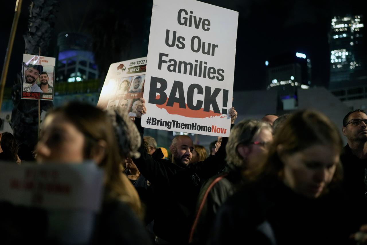 Mehrere Menschen stehen nebeneinander bei einer Demonstration. Ein Mann hält ein Plakat. Darauf steht "Give Us Our Families Back! #BringThemHomeNow". 