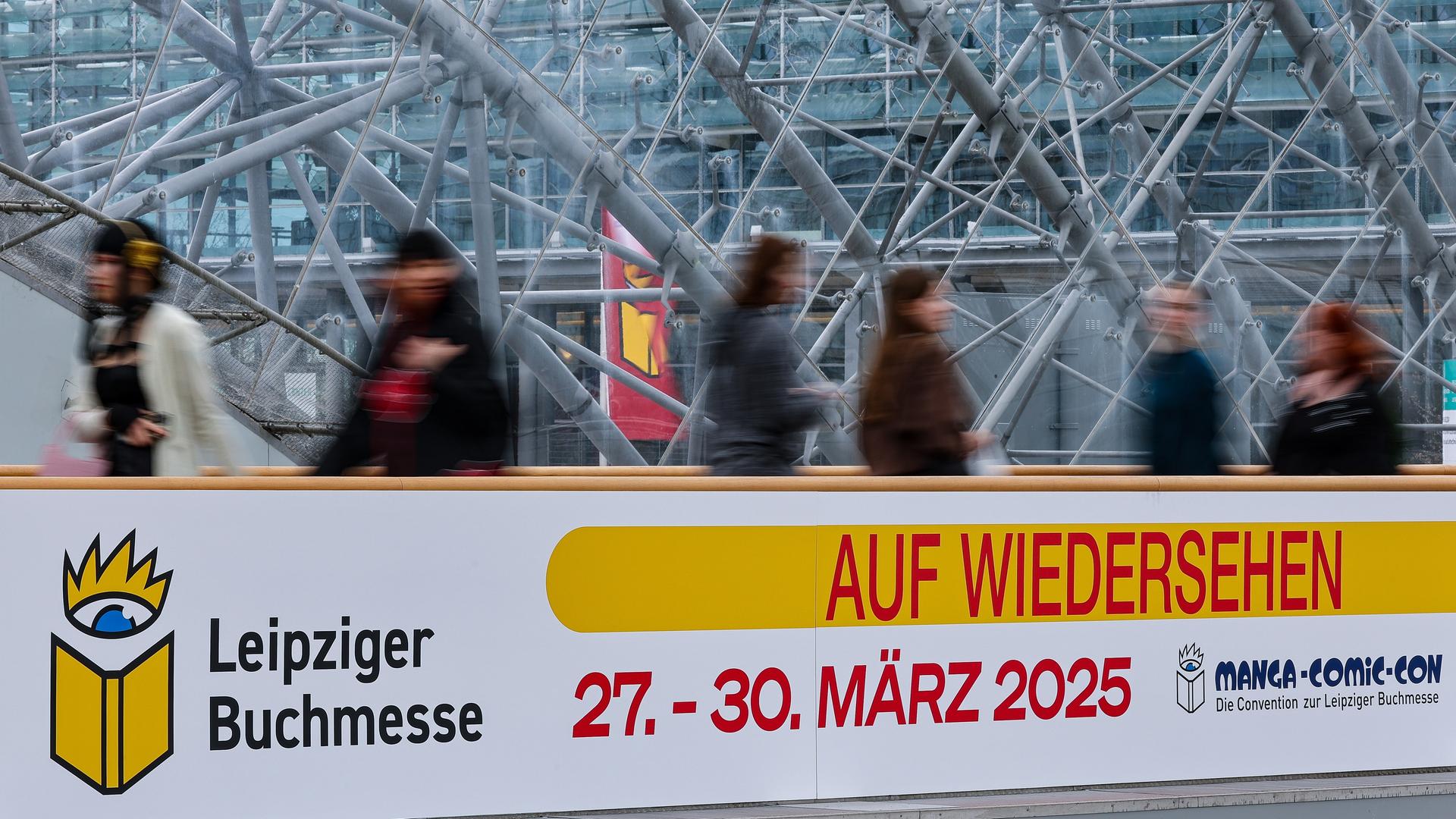 Besucher gehen auf der Leipziger Buchmesse an einem Schild "Auf Wiedersehen" entlang. A