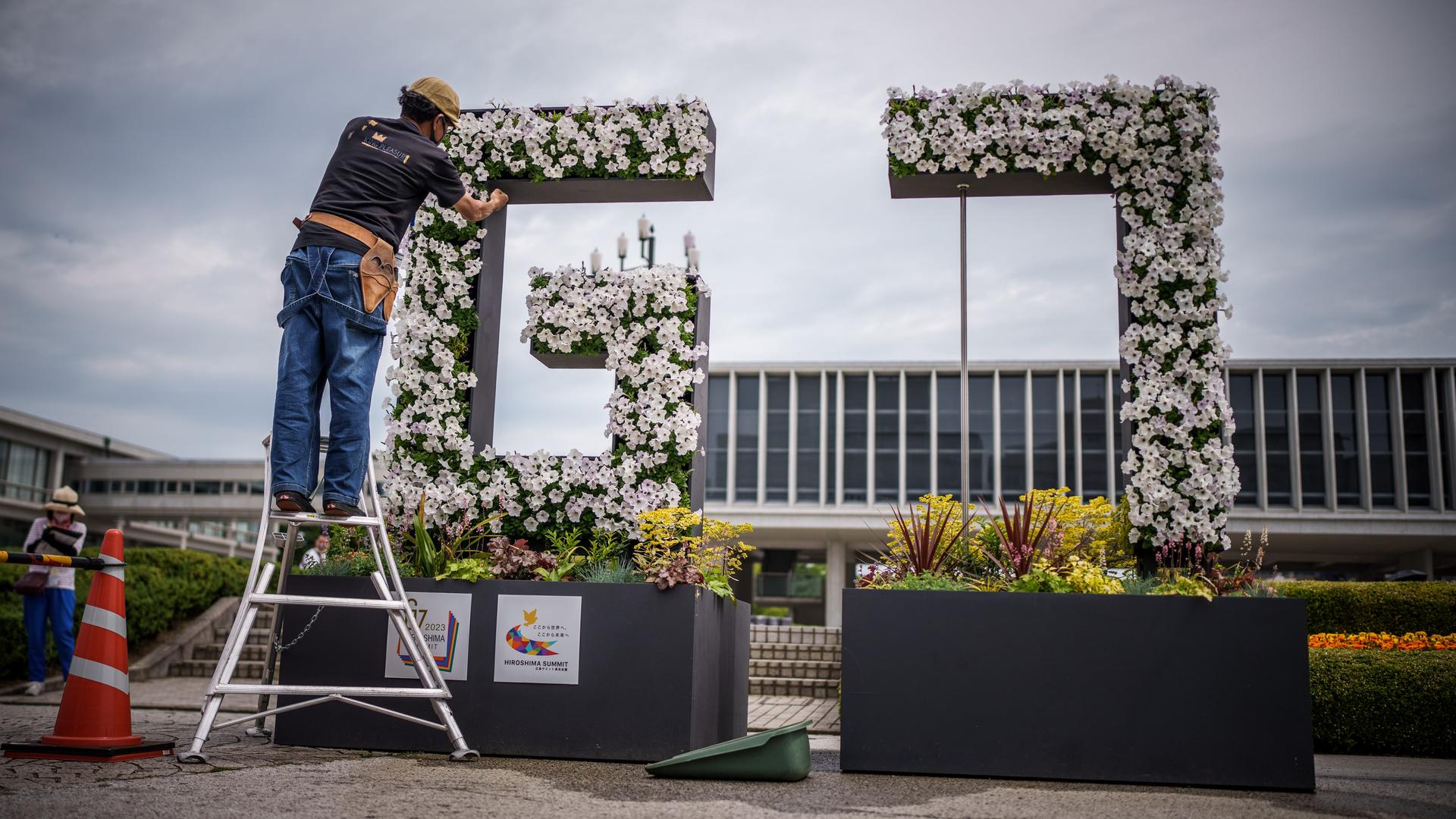 Ein Gärnter arbeitet im Hiroshima Peace Memorial Park an einem G7 Logo aus Blumen mit dem Genbaku Dome im Hintergrund. Ein Gärnter arbeitet im Hiroshima Peace Memorial Park an einem G7 Logo aus Blumen mit dem Genbaku Dome im Hintergrund.