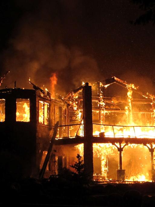 Ein Haus steht bei Nacht vollständig in Flammen, nur die Struktur des Hauses ist noch zu erkennen.
