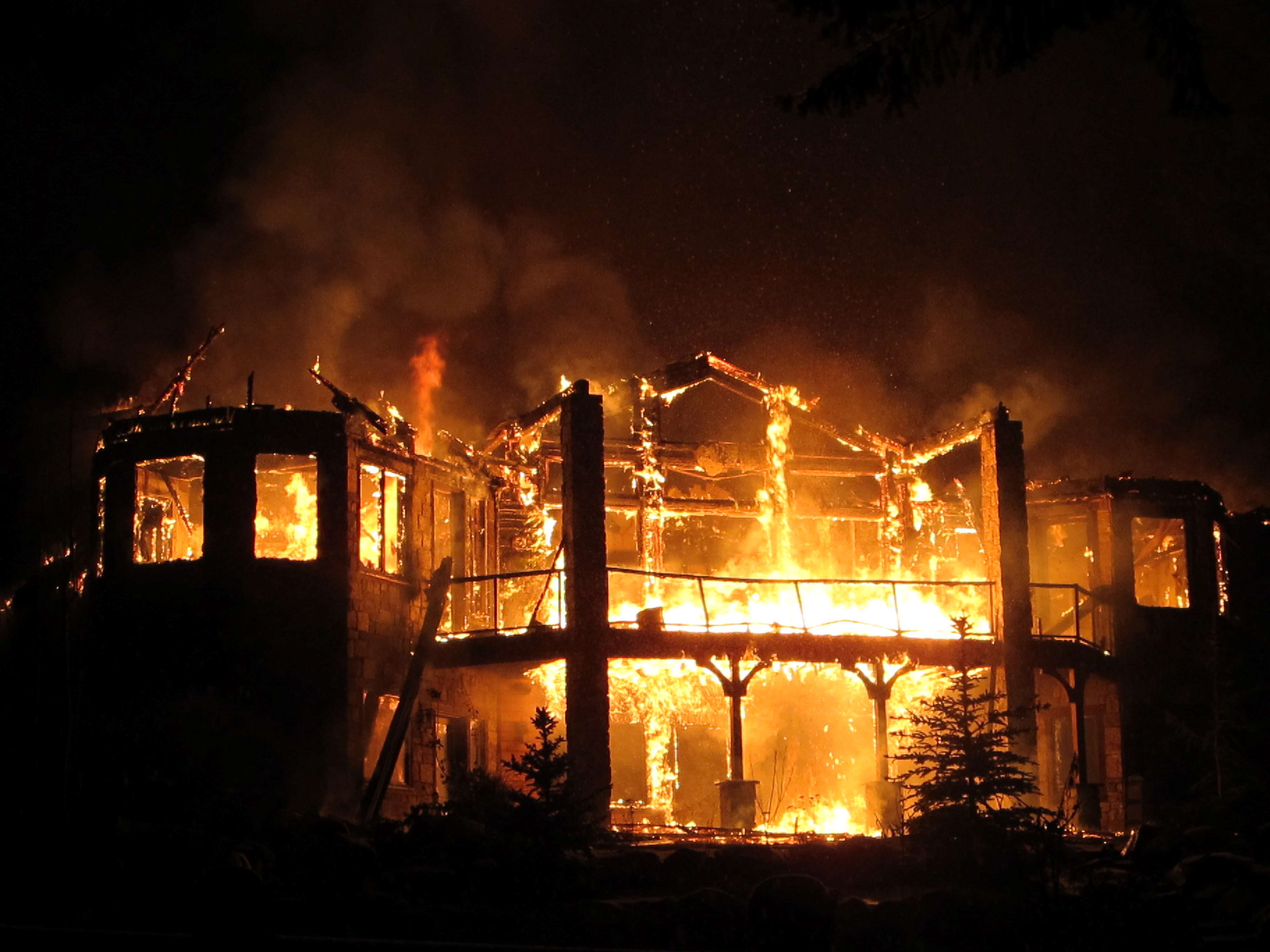 Ein Haus steht bei Nacht vollständig in Flammen, nur die Struktur des Hauses ist noch zu erkennen.