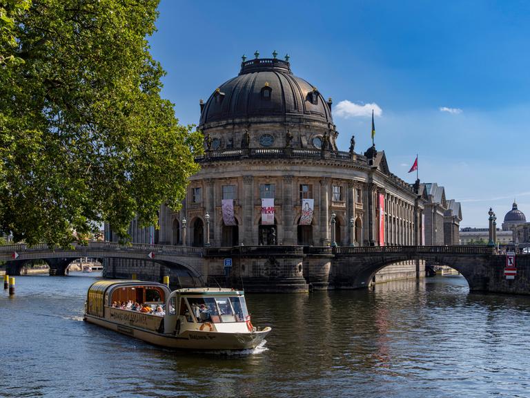 Blick auf die Spree mit Ausflugsboot und die dahinter liegende Berliner Museumsinsel mit dem Bode-Museum.