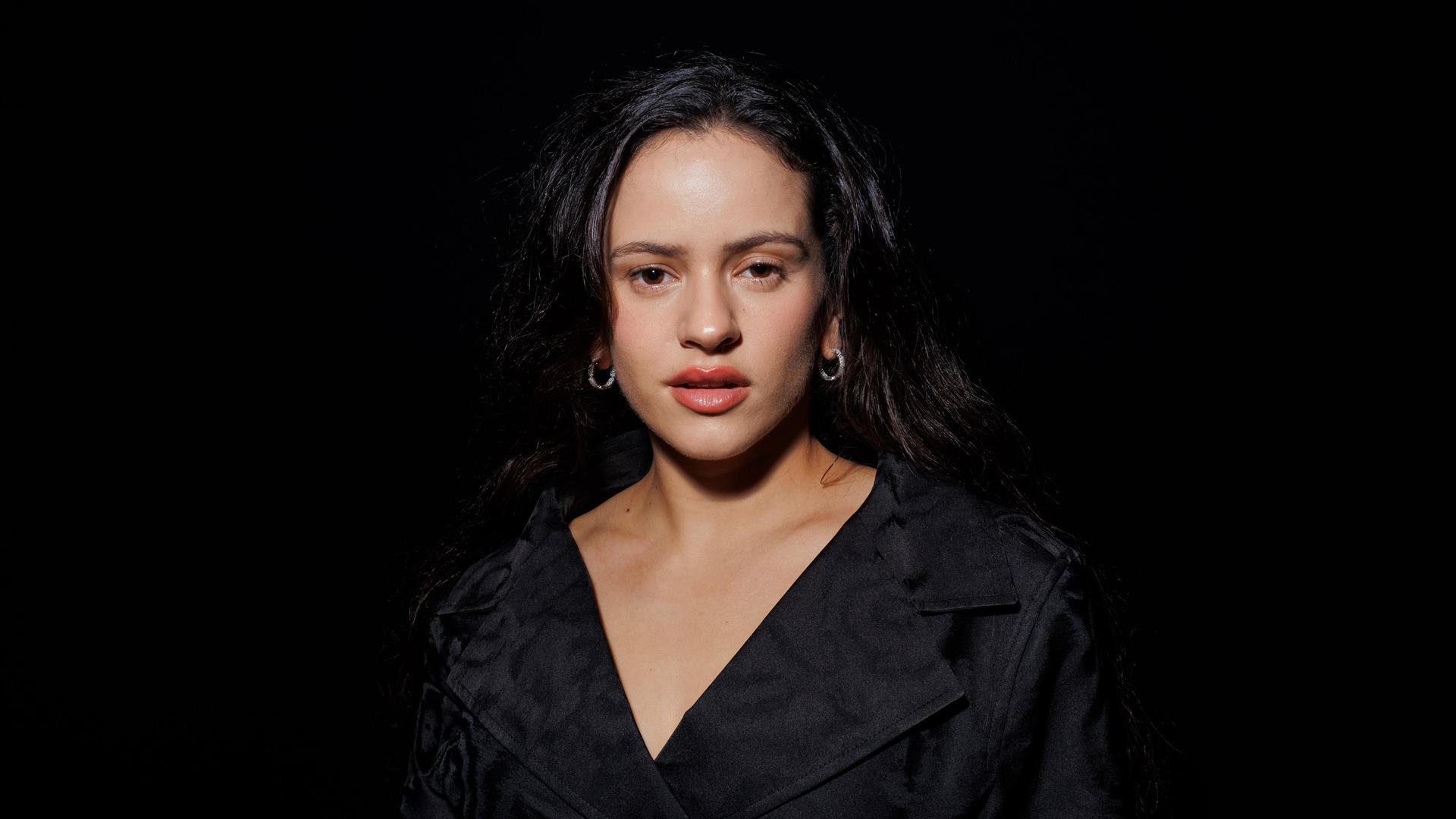 Die spanische Sängerin Rosalía auf einem Porträtfoto vor schwarzem Hintergrund. Sie trägt ein schwarzes Kleid, zu sehen sind vor allem ihr Gesicht und Dekolleté. Die spanische Sängerin Rosalía auf einem Porträtfoto vor schwarzem Hintergrund. Sie trägt ein schwarzes Kleid, zu sehen sind vor allem ihr Gesicht und Dekolleté.