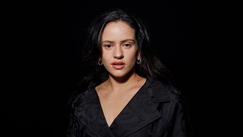 Die spanische Sängerin Rosalía auf einem Porträtfoto vor schwarzem Hintergrund. Sie trägt ein schwarzes Kleid, zu sehen sind vor allem ihr Gesicht und Dekolleté. Die spanische Sängerin Rosalía auf einem Porträtfoto vor schwarzem Hintergrund. Sie trägt ein schwarzes Kleid, zu sehen sind vor allem ihr Gesicht und Dekolleté.