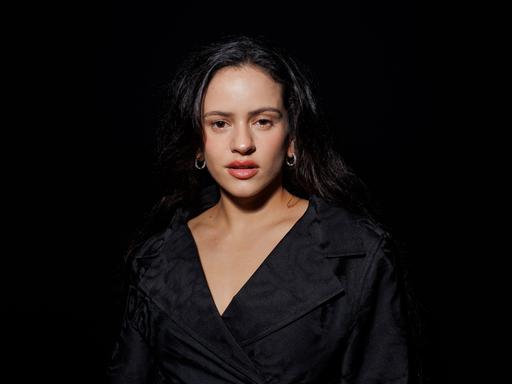 Die spanische Sängerin Rosalía auf einem Porträtfoto vor schwarzem Hintergrund. Sie trägt ein schwarzes Kleid, zu sehen sind vor allem ihr Gesicht und Dekolleté.