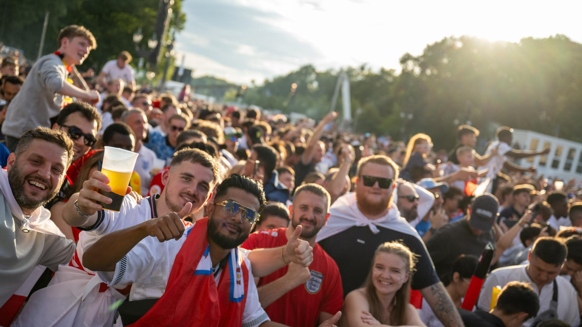 Fußballfans auf der Berliner Fanmeile stehen eng zusammen, heben Biergläser und lachen. Sie tragen Fanshirts.