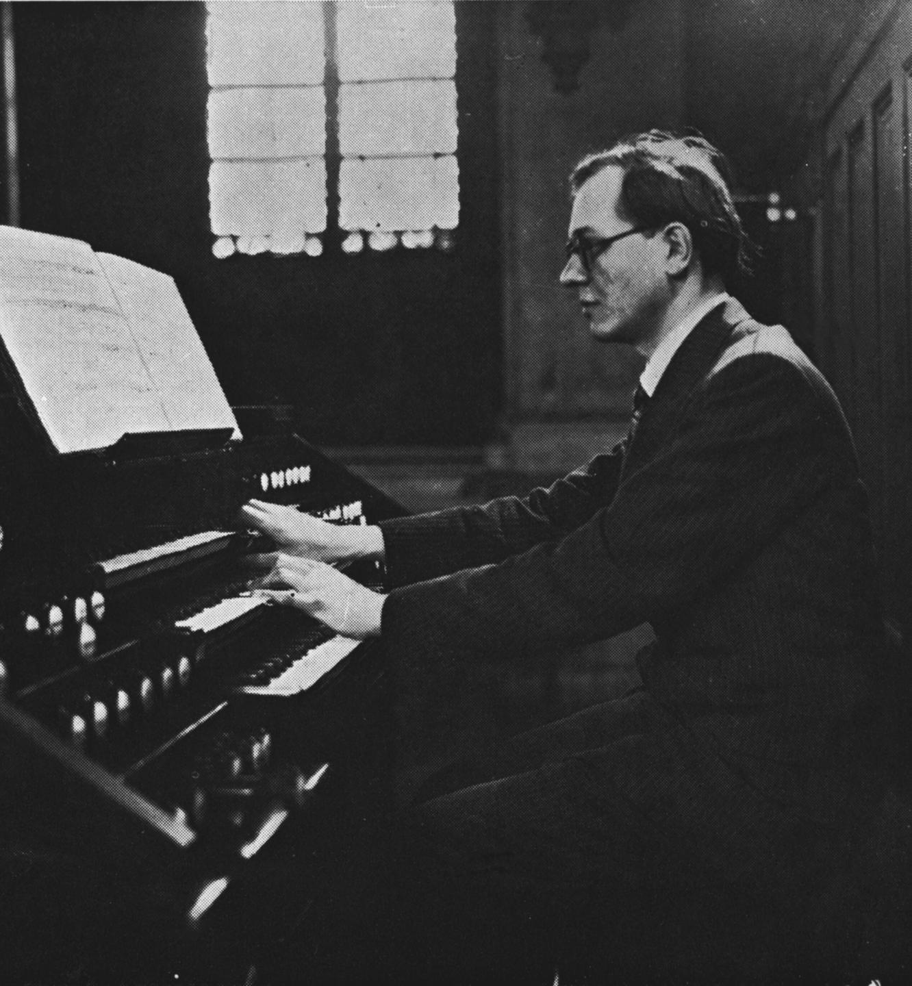 Olivier Messiaen sitzt als junger Mann mit Brille auf einer undatierten Fotografie in schwarz-weiß an einer Orgel.