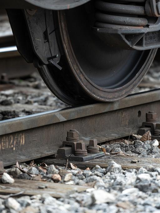 Nahaufnahme eines Zugrads, das über eine Metallschiene fährt. Unter der Schiene liegt Schotter, einzelne Steine sind gut erkennbar. Weitere Teile des Zuges sind nicht sichtbar.