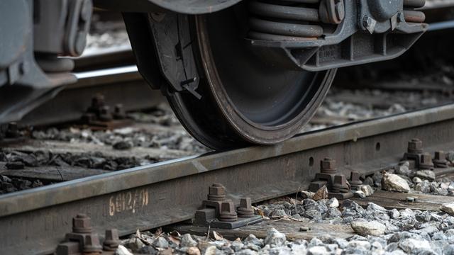 Nahaufnahme eines Zugrads, das über eine Metallschiene fährt. Unter der Schiene liegt Schotter, einzelne Steine sind gut erkennbar. Weitere Teile des Zuges sind nicht sichtbar.