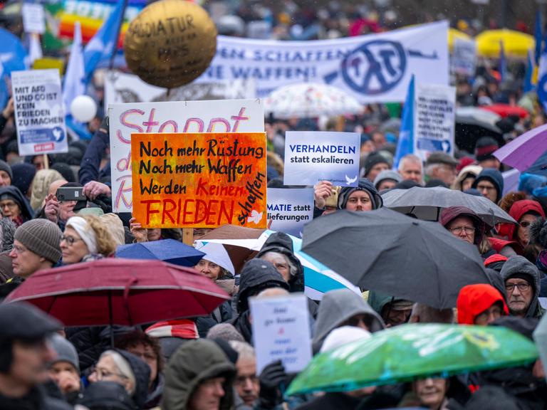 Zahlreiche Teilnehmer der Demonstration halten Schilder und Transparente in die Höhe. Am Brandenburger Tor in Berlin haben sich mehrere Tausend Menschen zu einer Kundgebung für Verhandlungen mit Russland im Ukraine-Krieg versammelt.