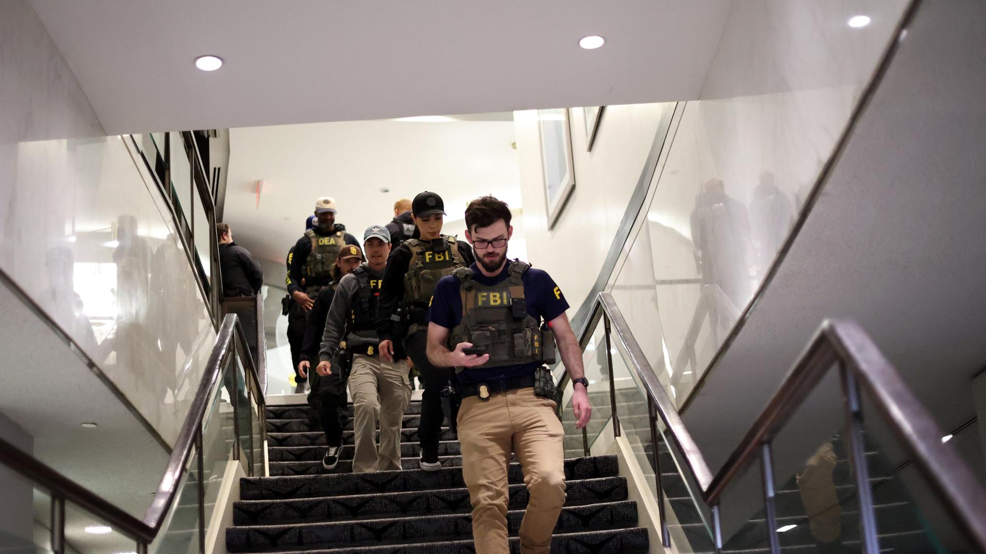 Mehrere bewaffnete Personen gehen eine Treppe herunter. Auf ihren Westen steht "FBI".