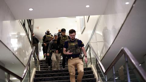 Mehrere bewaffnete Personen gehen eine Treppe herunter. Auf ihren Westen steht "FBI".