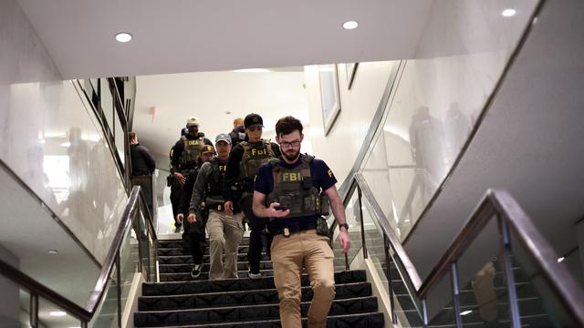 Mehrere bewaffnete Personen gehen eine Treppe herunter. Auf ihren Westen steht "FBI".