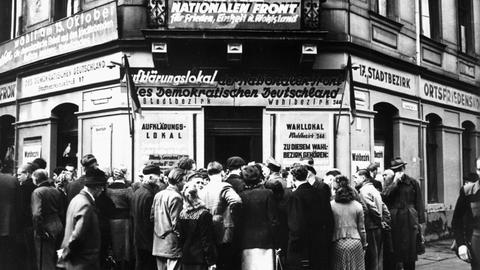Ein Schwarz-Weiß-Foto zeigt Menschen die am 12.10.1950 vor dem Aufklärungs- und Wahllokal Königsbrücker Straße 66 in Dresden über die Volkswahlen am 15.10.1950 diskutieren