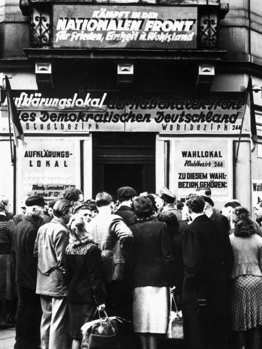 Ein Schwarz-Weiß-Foto zeigt Menschen die am 12.10.1950 vor dem Aufklärungs- und Wahllokal Königsbrücker Straße 66 in Dresden über die Volkswahlen am 15.10.1950 diskutieren