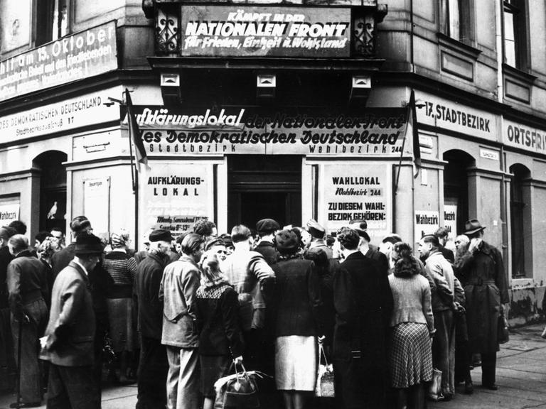Ein Schwarz-Weiß-Foto zeigt Menschen die am 12.10.1950 vor dem Aufklärungs- und Wahllokal Königsbrücker Straße 66 in Dresden über die Volkswahlen am 15.10.1950 diskutieren